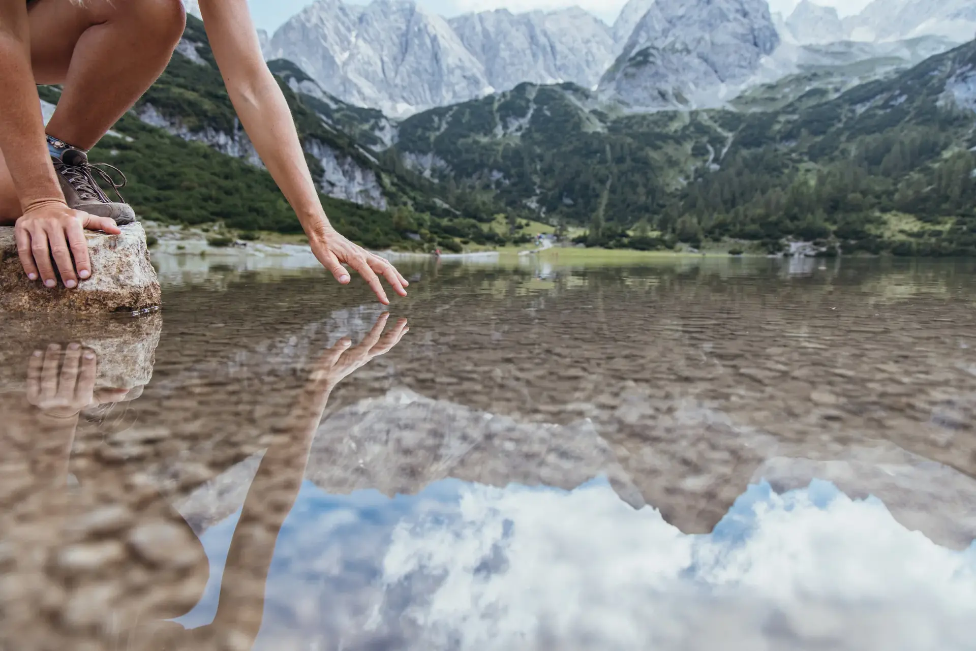 Hand berührt die Wasseroberfläche eines Bergsees